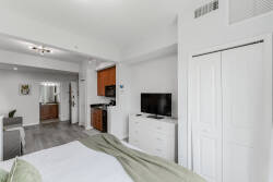 This stylish studio combines comfort and functionality, featuring a cozy bed with soft linens and a sleek kitchenette with warm wood cabinetry. The inviting light floods the space, creating a welcoming atmosphere for your stay.