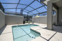 Discover your private oasis featuring a sparkling pool nestled within sleek walls that ensure both privacy and sunshine. Unwind in the spacious screened-in area on lounge chairs, soaking in the warm sunshine and clear blue sky.