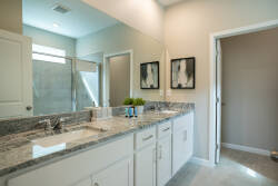 Step into this contemporary bathroom featuring elegant dual sinks with sleek granite countertops, framed art pieces that add a touch of sophistication, and abundant natural light filtering through the frosted window.