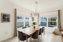 Gather in a bright dining area with a wooden table, cushioned chairs, large windows, soft curtains, modern chandelier, and pool views, creating a comfortable space for family meals during vacation.