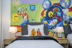 This cheerful bedroom features vibrant colors and playful decor, including a mural of beloved characters. With a cozy bed and plush pillows, it invites guests to relax in a bright and inviting atmosphere.
