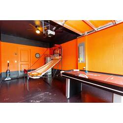 Have fun in a bold game room with a basketball arcade game, dart board, bright orange walls, black accents, sporty decor, and nearby air hockey for family entertainment.