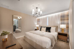 Step into a cozy bedroom, where soft beige tones complement the plush bedding and chic plaid curtains. A stylish chandelier casts a warm glow, while the elegant mirror adds depth, creating a welcoming ambiance for your stay.
