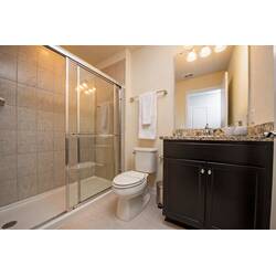 Refresh in a clean bathroom with a glass shower, neutral tile, granite vanity, dark cabinets, large mirror, soft lighting, and fresh towels for vacation comfort.