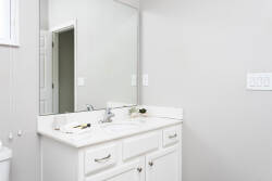 This bright and airy bathroom, with its sleek white vanity and large mirror, invites natural light in, creating a refreshing space for your daily routine with its minimalist design and subtle decor.