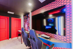 Experience a vibrant gaming oasis with sleek chairs and a colorful wall. Enjoy immersive entertainment on a large screen, and let the bold red doors add a fun touch to make your visit unforgettable.