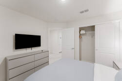 Experience comfort in this contemporary bedroom with its clean design, soft neutral tones, and cozy bed featuring a light blue comforter. Enjoy the sleek dresser and modern convenience of a mounted TV for your relaxation.