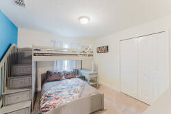 This cozy bedroom features a cheerful bunk bed ideal for kids or guests. The soft beige carpet and vibrant blue wall create a balanced atmosphere, enhanced by natural light for a warm and inviting space.