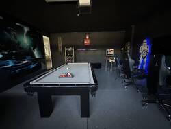 Enjoy a dark sci-fi themed game room with a pool table, arcade machines, gaming chairs, space mural, cue rack, and bold lighting, perfect for games and entertainment.