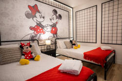 Experience a delightful bedroom featuring a whimsical Minnie Mouse mural that enhances the playful vibe. The cozy twin beds with crisp white linens and vibrant red accents create a lively, inviting space perfect for all guests.