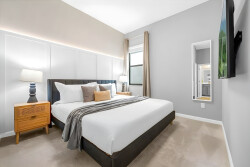 Enjoy the warm glow of natural light in this cozy bedroom featuring a plush king-sized bed. With its wood accents and soft gray tones, it’s the perfect retreat for relaxation.