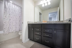 This bright and functional bathroom boasts a sleek granite countertop and a charming, patterned shower curtain. With ample storage in dark wood cabinetry, your essentials will stay organized for a clutter-free experience.