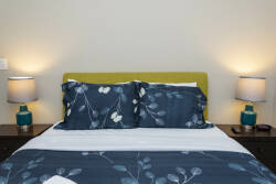 Enjoy restful nights in this cozy bedroom with a vibrant green headboard and deep blue floral bedding. Soft, ambient lighting from stylish lamps enhances the inviting atmosphere, perfect for relaxation and comfort.