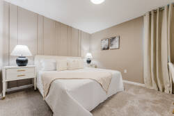 Welcome to this cozy bedroom, where soft beige tones create a calming atmosphere. Enjoy the plush carpet underfoot and minimalist decor, enhanced by elegant lamps on each nightstand for a warm evening glow as you unwind.