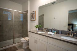 Bright and airy, this bathroom features a sleek double vanity with modern fixtures and a spacious glass-enclosed shower. The warm tones of the cabinetry complement the stylish decor, ensuring a refreshing start to your day.