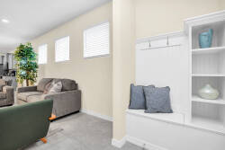 Welcome to a thoughtfully designed living area where soft gray sofas invite you to relax, bathed in natural light from multiple windows. A cozy reading nook with plush pillows and charming decor adds a personal, homey touch.