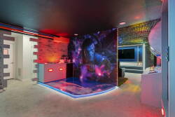 Experience a lively entertainment room with vibrant neon lights and a cosmic mural that sets an electrifying atmosphere. Its sleek, modern design and polished floor create the perfect space for gatherings or relaxation.
