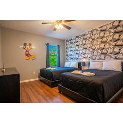 Enjoy a playful escape in this charming bedroom with two cozy beds dressed in crisp black linens. A cheerful Mickey Mouse mural brings whimsy, perfectly paired with stylish floral wallpaper that enhances the room's character.