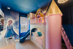 Welcome to a whimsical retreat featuring a castle-themed bunk bed with vibrant pink towers and a fun slide. The bold blue walls, decorated with enchanting characters, inspire adventure and creativity for young explorers.