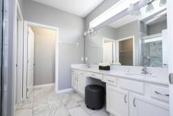 Step into a bright bathroom featuring sleek white cabinetry and elegant marble flooring that creates a clean, spacious feel. Large mirrors and ample lighting enhance the modern design, making it a refreshing start to your day.