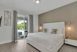 Rest in a bright bedroom with a white upholstered bed, soft bedding, modern bedside lights, gray curtains, wood flooring, and sliding glass doors with direct access to the patio.