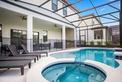 Discover an outdoor oasis with a sparkling pool and inviting hot tub, surrounded by sleek black loungers perfect for relaxation. Enjoy the airy space under a protective screen, ideal for unwinding or entertaining in comfort.