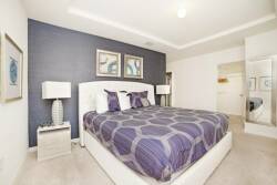 This cozy bedroom offers a plush king-sized bed with a chic purple geometric design, accompanied by stylish bedside lamps. The calming accent wall creates a perfect atmosphere for restful nights and relaxation.