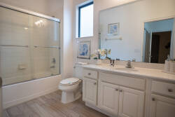 Bright and airy, this bathroom features a spacious vanity with sleek white cabinetry and subtle decorative touches. Natural light streams in through the window, illuminating the elegant tilework and creating a refreshing ambiance.