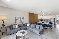 Relax in a bright open living area with cozy gray seating, a wall-mounted TV, warm wood accent wall, dining space, modern kitchen access, and soft decor for comfortable family time.