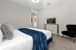 Welcome to this beautifully styled bedroom, where a plush white bed with a deep blue throw and chic pillows invites you to relax. The soft neutral walls and striking black accent chair create a cozy corner perfect for unwinding.