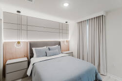 This cozy bedroom features a soft blue palette, accented by sleek nightstands and stylish sconces that provide a warm glow. The modern headboard and light-filtering curtains create a calm atmosphere, perfect for restful nights.