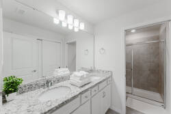 This bright bathroom boasts elegant granite countertops and crisp white cabinetry for a fresh atmosphere. Stylish lighting above the double sinks adds a modern touch, while the spacious shower ensures a comfortable experience.
