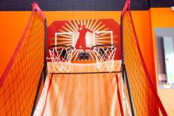 Step into a vibrant game room with energizing orange walls and a striking mural. Enjoy friendly competitions at the dual basketball hoops, making it perfect for fun-filled evenings with friends or family.