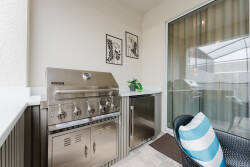Savor outdoor dining in our grilling area, featuring a sleek stainless steel barbecue and cozy striped cushion seating. Large windows bring in natural light, creating a warm and inviting atmosphere for your culinary experience.