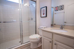 This bright bathroom offers a spacious walk-in shower with sleek glass doors and modern tile work. Light cabinetry and contemporary fixtures create a clean, refreshing atmosphere, ideal for your daily routines.