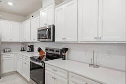 Cook with ease in a bright modern kitchen with white cabinets, stainless steel appliances, spacious counters, a large island, soft lighting, and an open view to the living room, perfect for family meals during vacation.