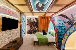 Enter a vibrant bedroom with dragon murals and warm wooden accents, creating a whimsical atmosphere. Enjoy the cozy bed with a soft green throw and modern lighting, perfect for relaxing after your day's adventures.