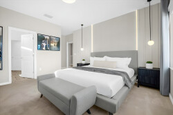 Experience a beautifully designed bedroom with a plush gray bedframe and cozy layered bedding for restful nights. Soft beige walls and warm lighting create a tranquil ambiance, while stylish artwork adds a personal touch.