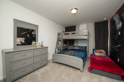 This cozy bedroom is bright and inviting, featuring a stylish bunk bed and a twin-sized daybed, ideal for family or friends. The soft neutral carpet pairs beautifully with sleek gray furniture and vibrant bedding for a fun touch.