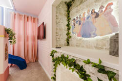 Step into a whimsical corner adorned with playful princess artwork and lush greenery, creating a cheerful atmosphere. The soft pink curtains add a touch of warmth, while the cozy carpet invites you to relax and enjoy.