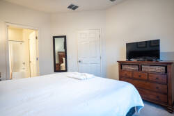 Experience comfort in this bright bedroom, featuring a soft white bedspread that invites relaxation. The dark wood dresser adds warmth, while the mounted TV offers entertainment options, making your stay both cozy and convenient.
