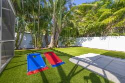 Step outside to discover a bright, lush yard framed by tall palm trees, where vibrant blue and red loungers await you. The plush green grass invites relaxation under the sun, creating a perfect spot for leisurely afternoons.