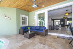 Step into a relaxing lounge area, where a stylish blue sectional invites you to unwind. The warm wooden ceiling and natural stone flooring create a cozy atmosphere, seamlessly connecting to the bright indoor space just beyond.