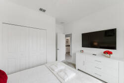 This bright bedroom features crisp white walls that create an airy feel, complemented by sleek, modern furniture. The wall-mounted TV offers entertainment, while the tasteful red accents add a pop of color, inviting relaxation.