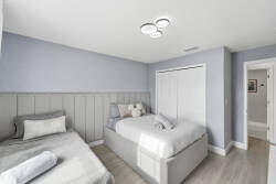 Experience tranquility in this serene bedroom with two cozy beds dressed in soft linens, soothing light blue walls, and elegant wood accents. Natural light floods the space, offering a bright, airy ambiance for restful nights.