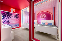 Step into a vibrant escape with striking pink walls and playful decor, featuring a dreamy mural of palm trees. Each bed is adorned with cozy blue accents, creating a cheerful ambiance perfect for relaxation and fun.
