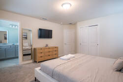 Welcome to a cozy bedroom with a plush gray bed and soft linens, complemented by a stylish wooden dresser. Natural light bathes the room, creating a calming atmosphere, while a sleek TV provides entertainment for your stay.