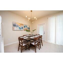 Share meals in a bright dining area with a set table, wooden chairs, modern chandelier, soft wall art, fresh greenery, white curtains, and easy patio access for vacation moments.