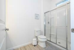 This bright and airy bathroom boasts sleek glass shower doors and warm wood-tone flooring, creating a fresh atmosphere. Natural light streams in, enhancing the modern decor for a refreshing start to your day.
