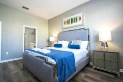 This beautifully styled bedroom features a plush upholstered bed with crisp white linens and vibrant blue accents, complemented by warm wooden flooring and soft bedside lamps, creating a relaxing and cozy atmosphere for your stay.